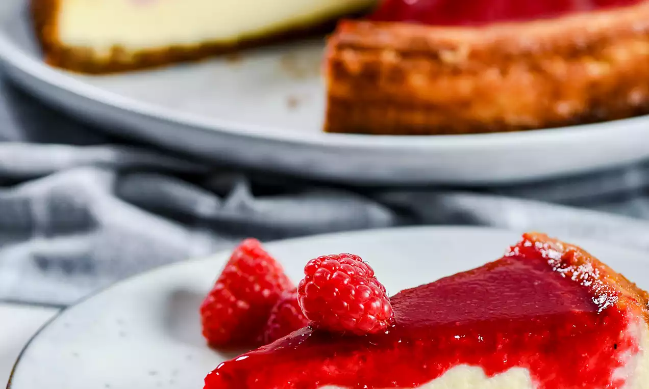 Picture - Bakad cheesecake med gyllene botten, krämigt lager och glansig hallonspegel, toppad med färska hallon på vita tallrikar